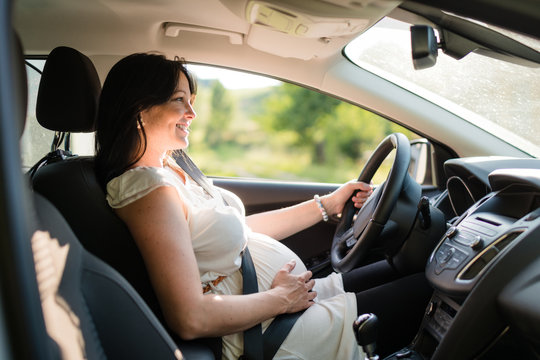 Pregnant woman driving her car, wearing seat belt.