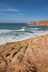 Fototapeta na wymiar red soil rocks on colorful amado beach with waves on atlantic coastline, algarve, portugal