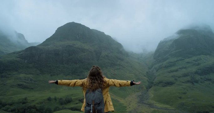 Woman with arms raised on in stormy weather looking at view of Mountain Hiker Girl lifting arm up celebrating scenic landscape enjoying vacation travel adventure nature Glen Coe Scotland