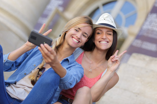 cheerful tourist female friends taking photos of themselves