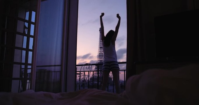 Young tourist woman stretching at sunrise on hotel terrace with view of Eiffel Tower Paris arms raised enjoying european travel adventure celebrating beautiful city 