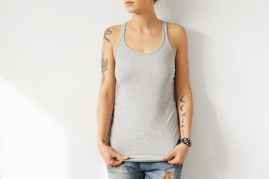 Online shopping. Clothes and apparel. Model posing in blue ripped jeans and stylish grey tank top with cope space for promotional content. Caucasian girl with perfect body trying on trendy clothing