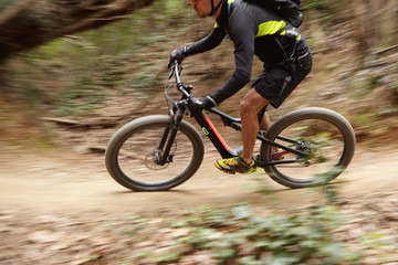 Freeze action of cyclist dressed in sportswear speeding along mountain trail in forest on his...