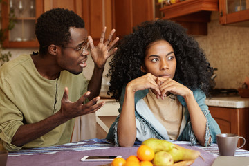 People and relationships concept. African American couple arguing in kitchen: man in glasses...