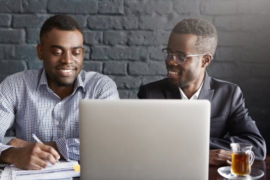 People, Business, Teamwork And Cooperation Concept. Two African American Corporate Workers In Formal Clothing Working Together On Common Presentation On Generic Laptop Computer In Modern Office