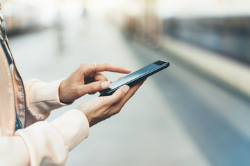 Enjoy travel. Young woman waiting on station platform with backpack on background electric train using smartphone. Tourist texting message and plan route of railway, railroad transport concept