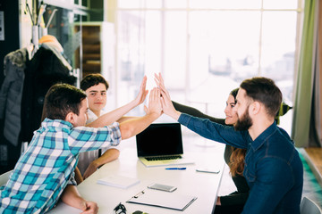 Young smart people are giving high five and smiling while sitting on the table in the modern library