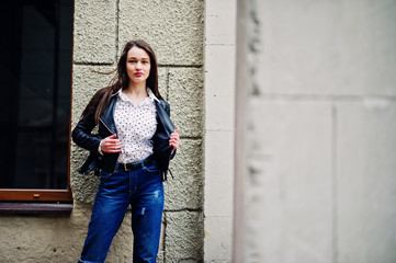 Portrait of stylish young girl wear on leather jacket and ripped jeans at streets of city. Street fashion model style.