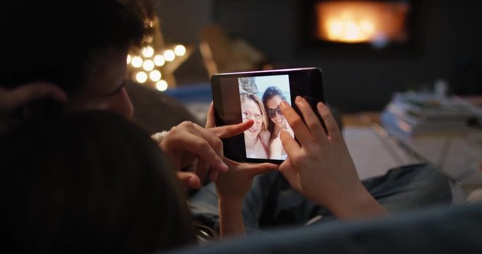 Closeup of couple using digital tablet by fireplace viewing travel photos on touchscreen browsing social media sharing wanderlust inspiration on digital device