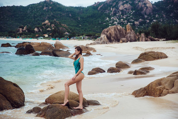 Young beautiful girl with an excellent figure posing on a tropical beach. Portrait of sexy woman in blue bikini swimwear. Concept of travelling and lifestyle