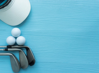 Golf clubs, golf balls, cap, on blue wooden table, with copy space.
