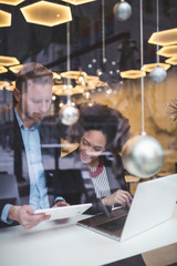 Multi racial business man and woman working together in modern cafe or restaurant. View from street through window glass.