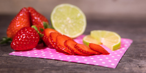 Erdbeeren ganz und aufgeschnitten mit Limette auf Holz