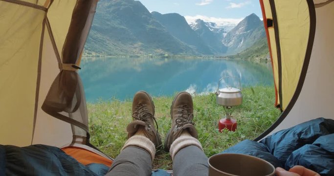 Camping woman lying in tent close up of girl feet wearing hiking boots drinking warm drink relaxing on vacation POV