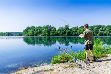 Angelabenteuer, Karpfenangeln. Angler fischt mit Karpfenfischtechnik an einem schönen Sommertag mit hellblauem Himmel