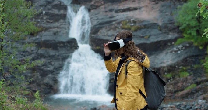 Adventurous Young traveler woman at waterfall wearing virtual reality headset watching 360 video imagination concept