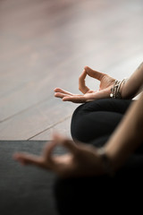Close up of mudra gesture, performed with female fingers, yogi woman meditating in lotus pose, wearing wrist bracelet, sitting in Padmasana exercise, vertical photo. Meditation session concept - obrazy, fototapety, plakaty