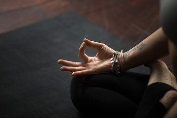 Close up of young woman hand with tattoo and wrist bracelets practicing yoga, sitting in Padmasana...
