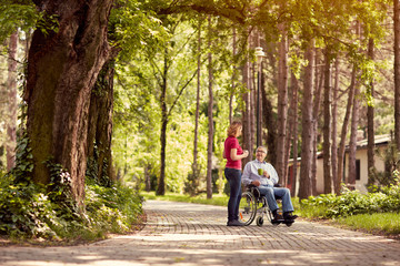 woman visiting her disabled father in wheelchair and enjoying time together in the park.