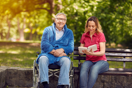 Spending time together reading book outdoor daughter and smiling disabled father in wheelchair.