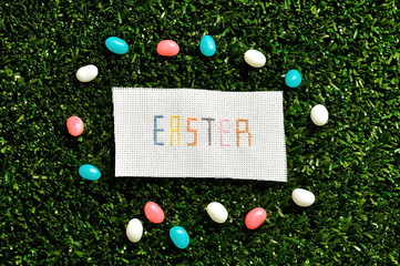 Easter cross stitched on textile isolated on artificial grass displayed with jelly beans