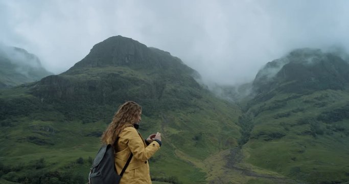 Woman taking photo of misty mountain valley smartphone photographing scenic landscape nature background view enjoying vacation travel adventure Glencoe Valley Scotland