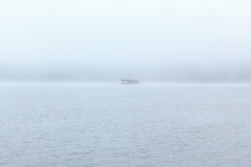 Floating wooden raft house on river with foggy background.
