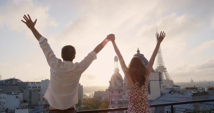 Young tourist couple stretching in morning on hotel balcony with view of Eiffel Tower Paris arms raised enjoying european travel adventure celebrating beautiful city sightseeing exploration