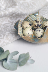 Table setting with decorative plate, green twig, linen napkin and quail eggs. Prepare to Easter. Toned in cold scale