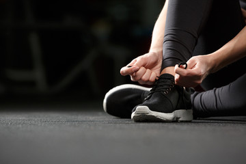 Cropped image of young fitness lady tie laces in gym.