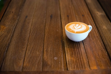 Latte art coffee in white mug on wood table in coffee shop.