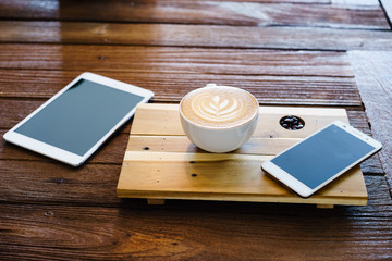 latte art coffee with smartphone or tablet on wood table.