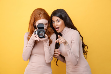 Cheerful young african woman pointing while redhead lady photographing