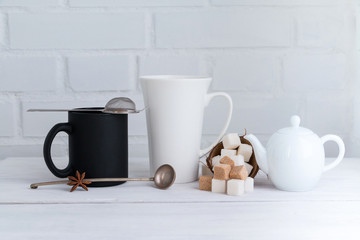 Fototapeta na wymiar White and black coffee and tea mugs with sugar cubes and teapot on wooden table. White background. Copy space.