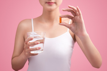 Young asian beauty young woman eating pills and drinking water on pink background.
