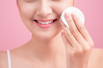 Obraz na płótnie Canvas Gorgeous young woman holding cotton pad and smiling in taking care of her face for fresh healthy skincare on pink background