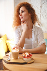 Amazing redhead young lady sitting in cafe while eating dessert.