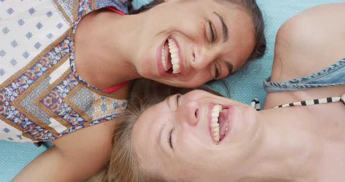 Top view of teenage girl friends lying on back smiling laughing at beach direct from above