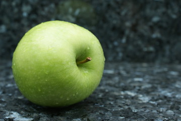Einzelner grüner Apfel vor schwarzem Mamor