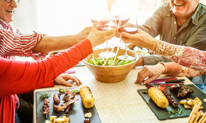 Senior friends cheering with red wine at barbecue lunch indoor