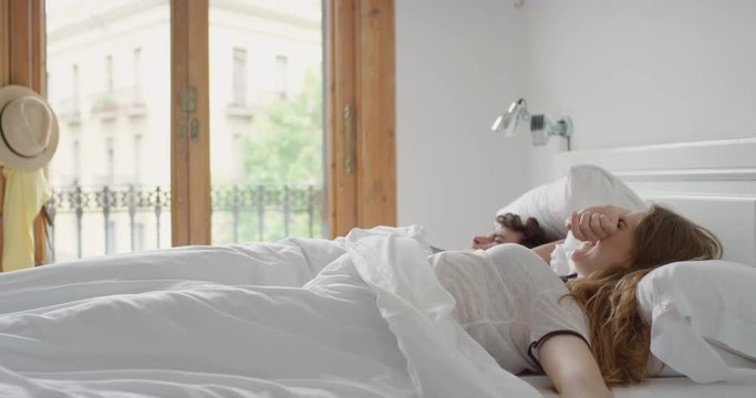 Young couple waking up in bright sunny room laughing and cuddling 