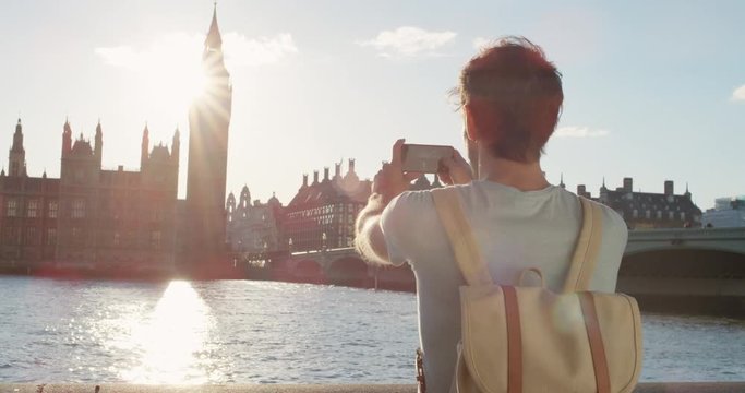 Tourist Man taking photo of Big Ben London with smart phone technology for social media at sunset enjoying vacation travel adventure