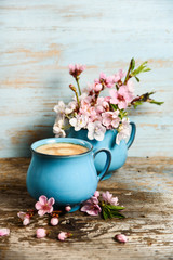 Coffee in old blue cup with pink blooming flowers on grunge wood background. good morning post card, banner design 