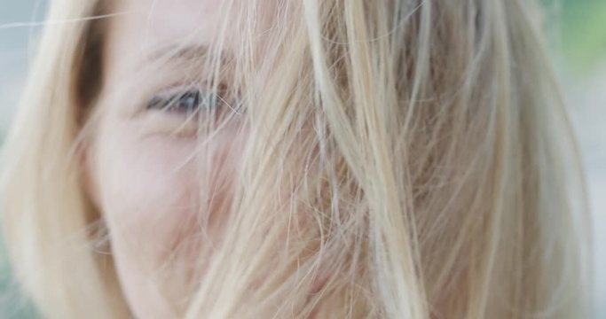 Close up portrait of beautiful young woman smiling hair blowing in wind outdoors slow motion