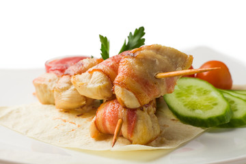 chicken on a skewer, baked in bacon, rests on a pita with cucumber, cherry tomatoes, parsley and savory sauce, white background, isolated