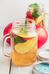 Tea with ice, slices of red apples and cinnamon sticks in a glass jar with a lid.