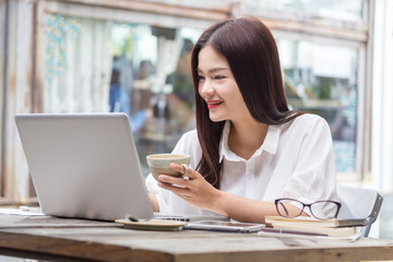 Fototapeta na wymiar young attractive asian business woman using her computer and holding a cup of coffee