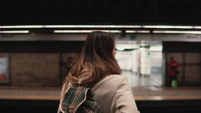 Brunette woman standing on railway station and waiting for her train. Girl in underground at evening looks on fast trams