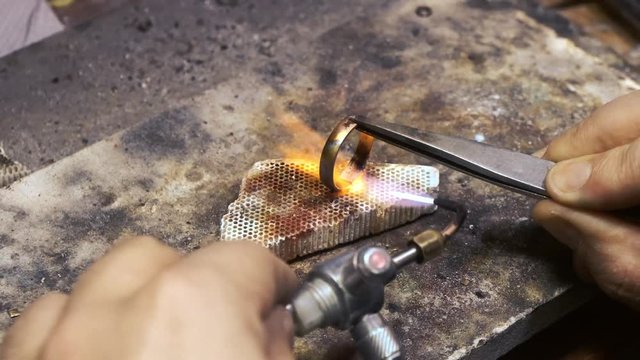 Process of soldering gold ring by torch. Production and making manufacturing, factory, cast craft design, process precious gold jewelry, jewels, ring jeweler, goldsmith in workshop.