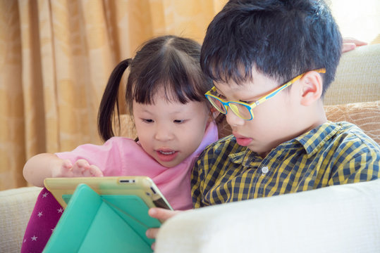Asian siblings playing games on tablet computer together
